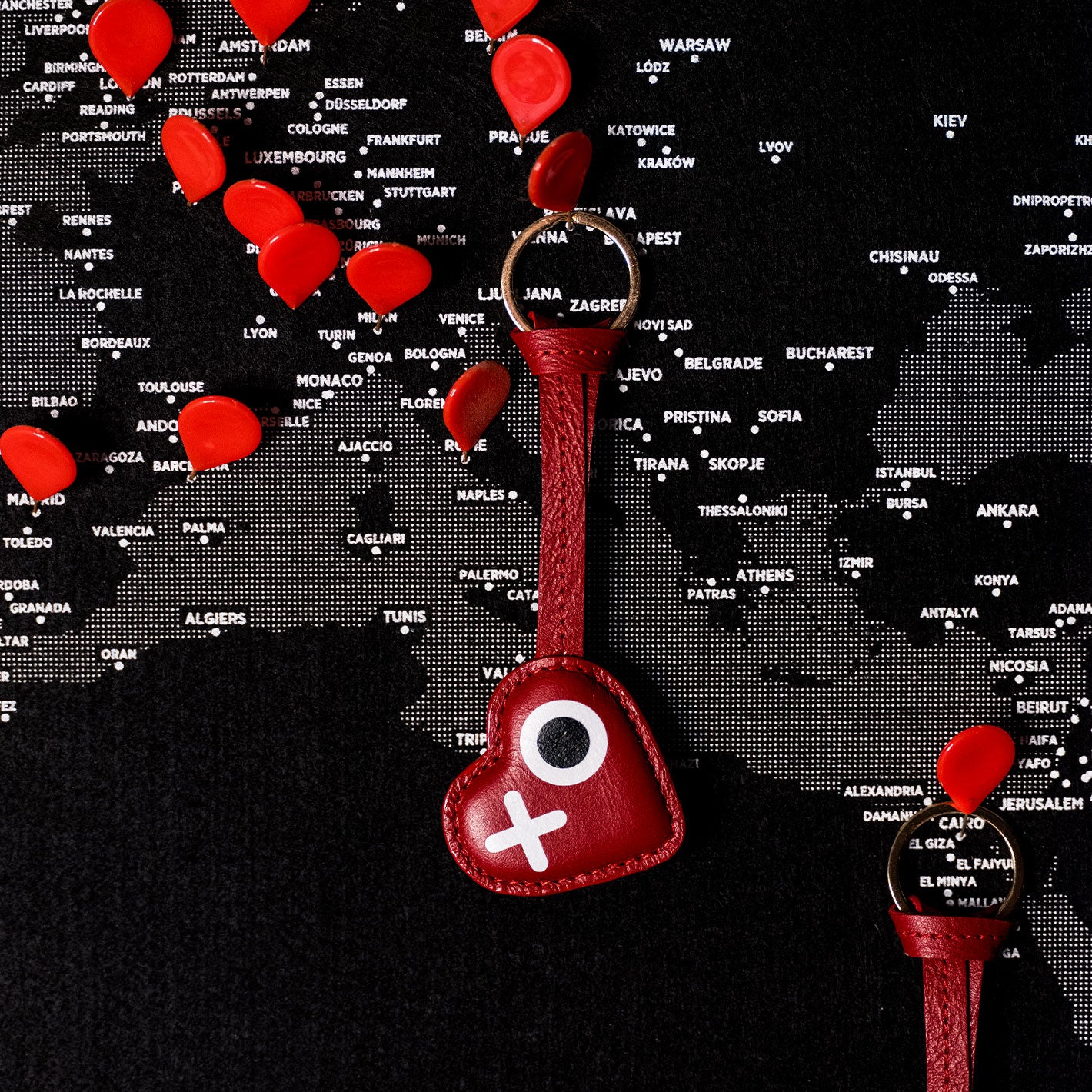 Red heart-shaped keychain with a white cross on a world map background