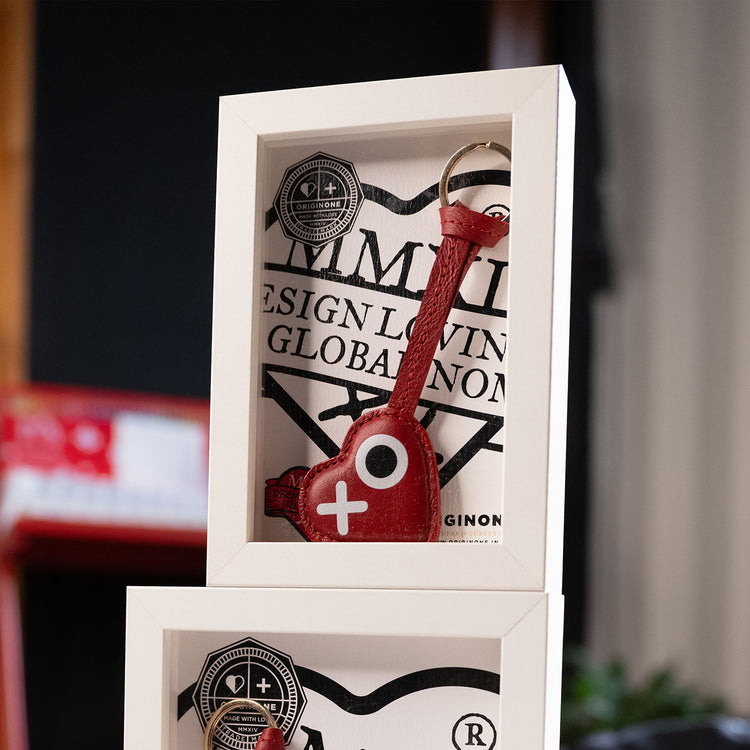 Red keychain with a white plus sign in a white box with branding on a blurred background