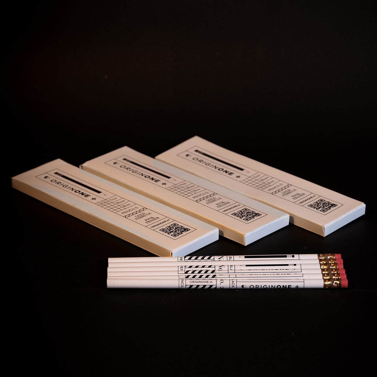 Three white Origin One brand pencils arranged diagonally on a black background, with 6 pencils in front showing its gold ferrules and red erasers.
